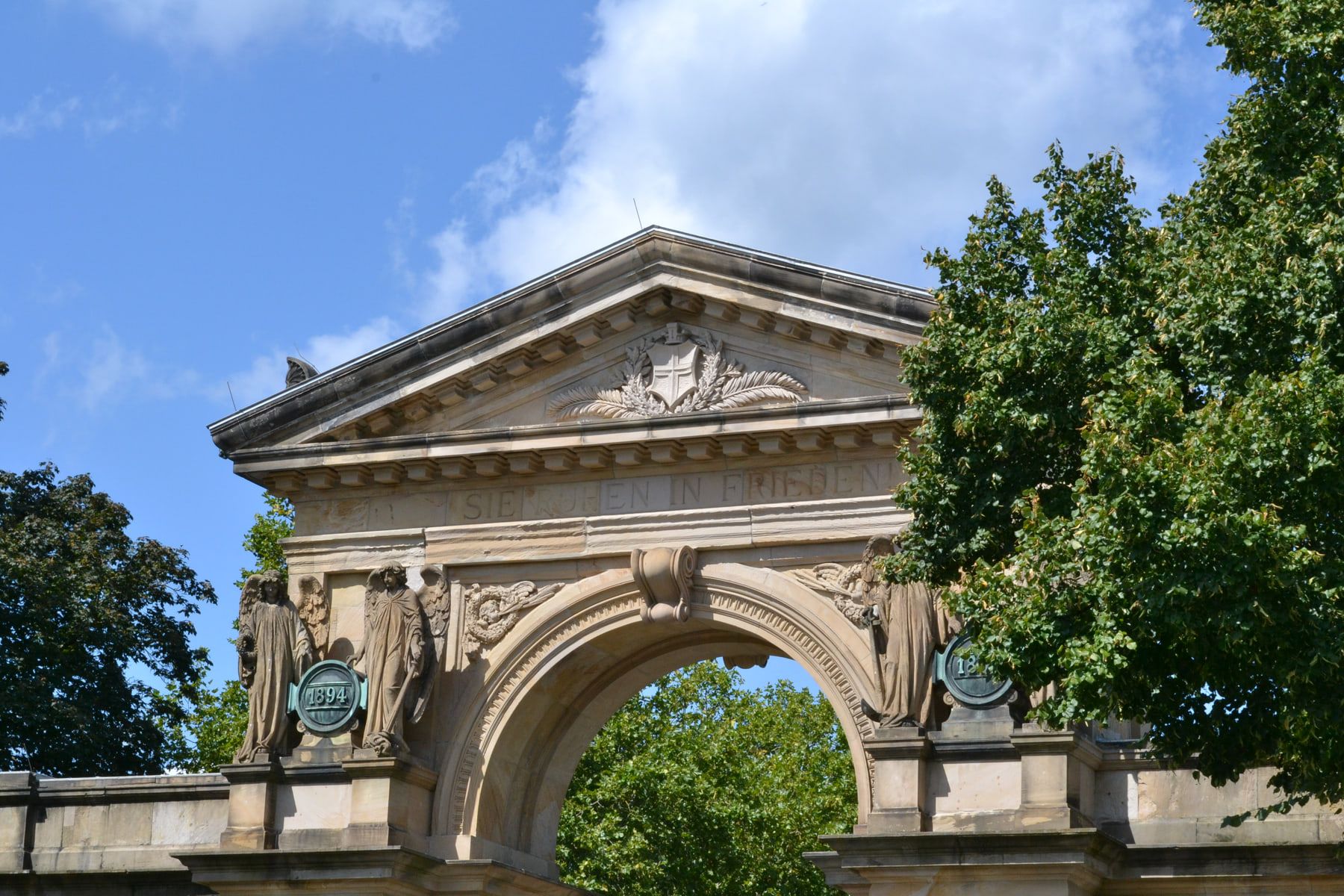 Skulpturengeschmückter Sandsteinbogen des Haupteingangs vor blauem Himmel auf Hauptfriedhof Freiburg