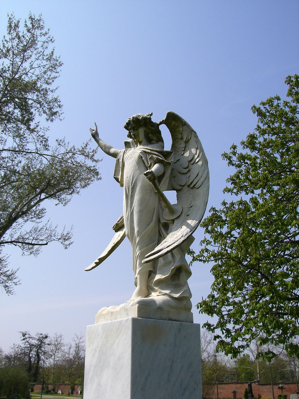 Weiße Engelsfigur am Urnenfeld mit erhobener Hand und ausgebreiteten Flügeln auf Hauptfriedhof Freiburg